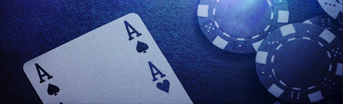 Close-up of stacked casino chips resting beside a face-up playing card on a dark blue textured surface, moody dramatic lighting with deep shadows and a quiet club atmosphere.